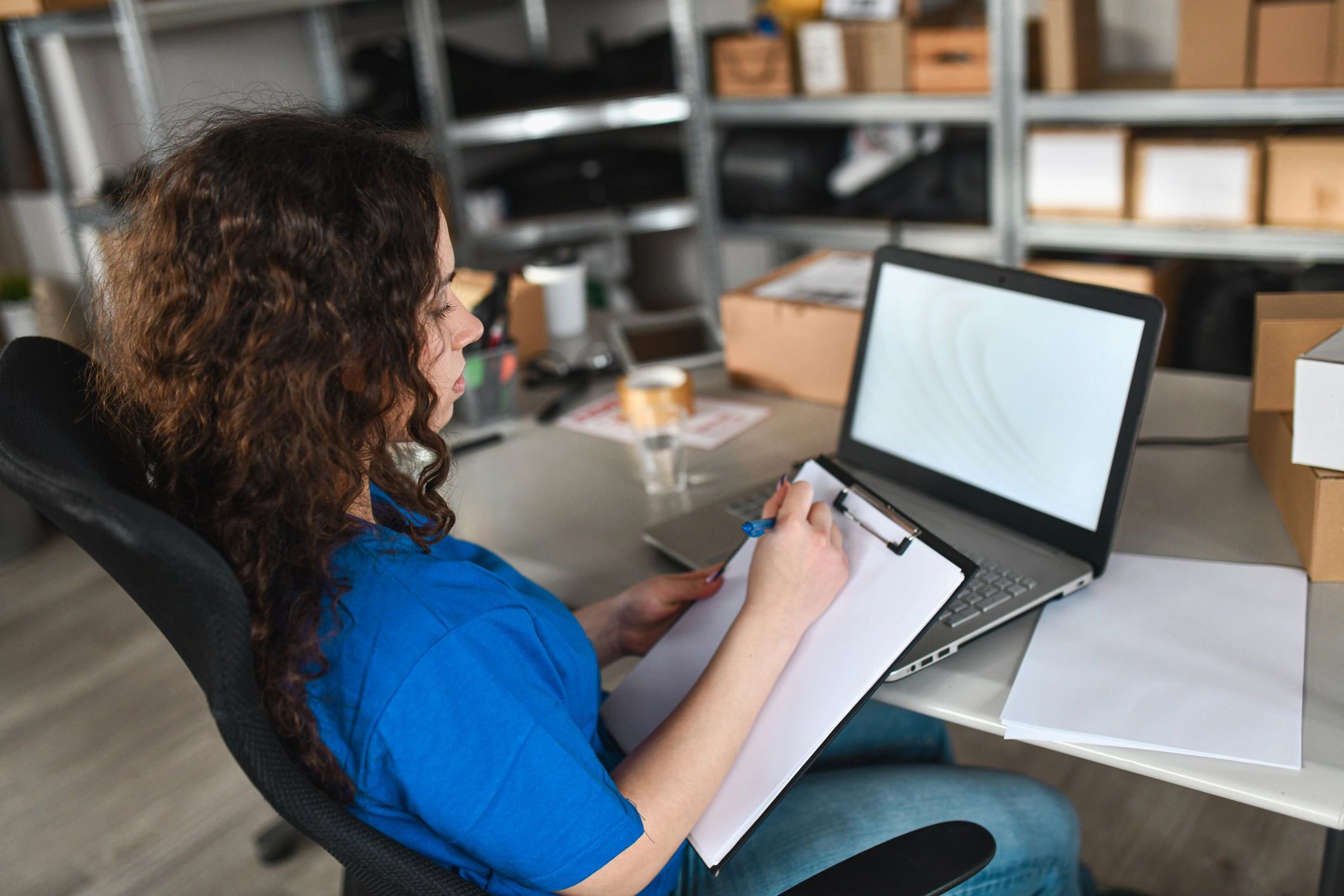 Employee reviewing shipment paperwork at a desk with a laptop